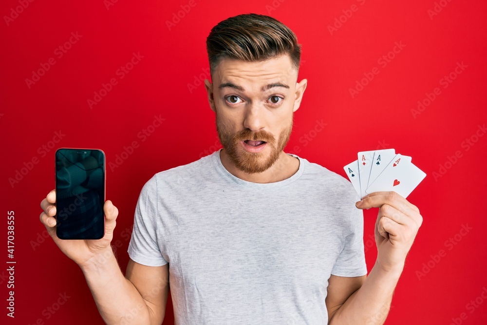 Young man looking confused holding gambling cards and mobile