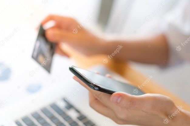 Hender holder et bankkort og en telefon for å betale på nett